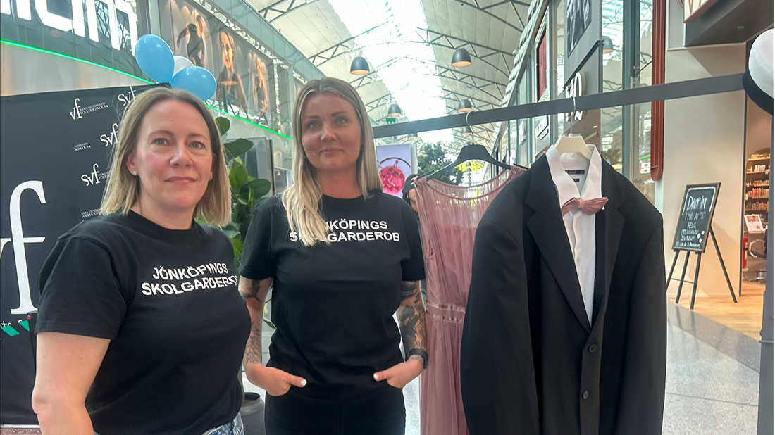 Två leende kvinnor i svart t-shirt med texten "Jönköpings skolgarderob" tittar in i kameran och ler