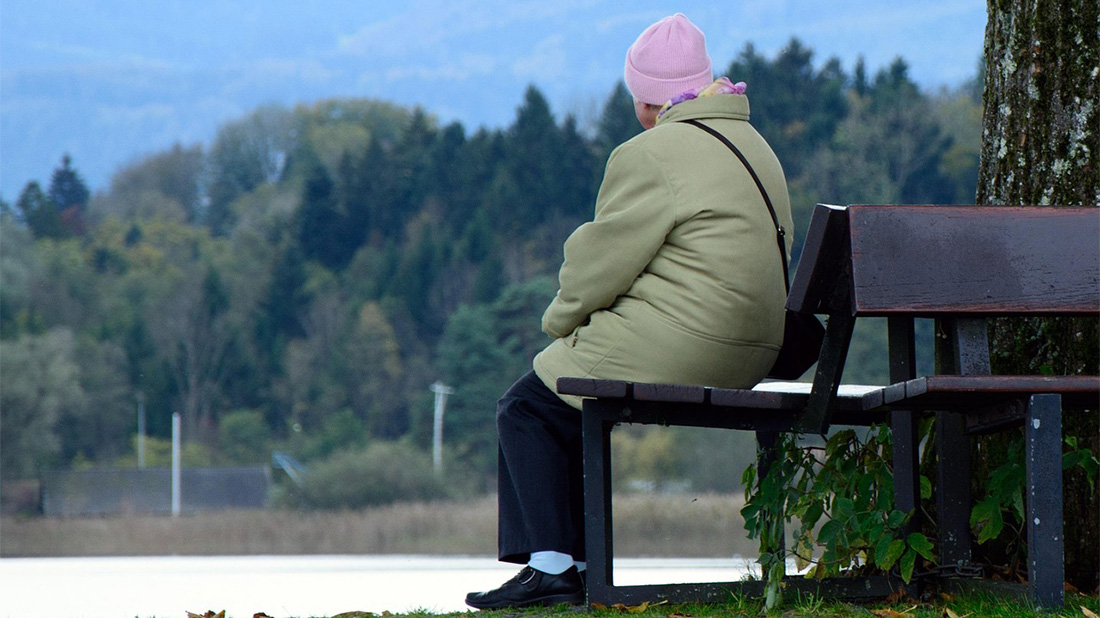 äldre dam som sitter på en bänk ute